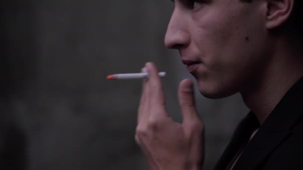 Привлекательный парень в черной куртке курит сигарету медленно — стоковое видео