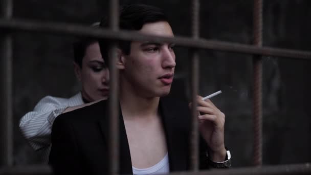 Beautiful lady stands behind handsome man smoking cigarette — Stock Video