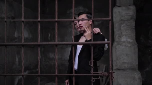 Mann raucht Zigarette und Blondine umarmt sich hinter rostigem Gitter — Stockvideo