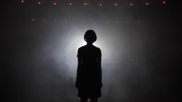 Silhouette di donna che cammina verso una luce intensa nel fumo — Video Stock