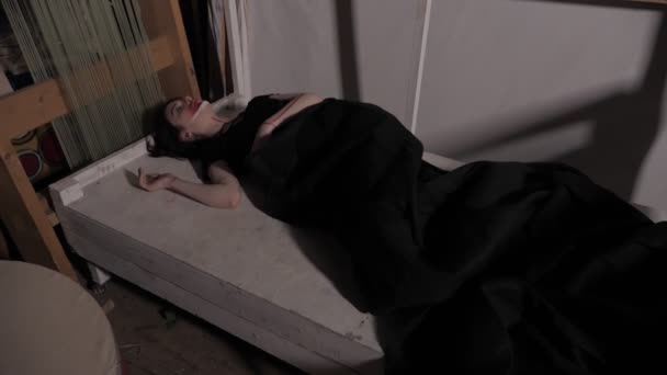 Νεαρή γυναίκα με σκούρο κουβέρτα στηρίζεται σε παλιό ξύλινο κρεβάτι — Αρχείο Βίντεο