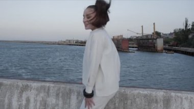 Kadın rıhtımda oturuyor ve deniz limanına gülüyor.