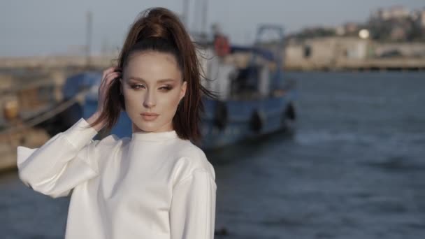 Young woman straightens ponytail against old boat and sea — Stock Video