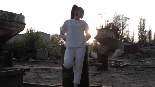 Lady leans on petrol tank against abandoned stuff at sunset — Stock Video