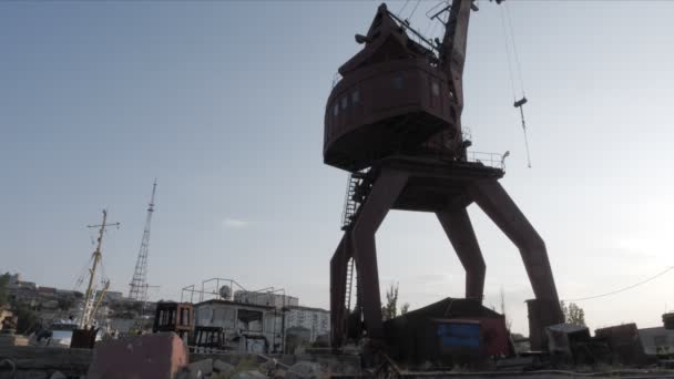 Señora camina a lo largo del puerto pasado enorme grúa vieja contra la puesta del sol — Vídeo de stock