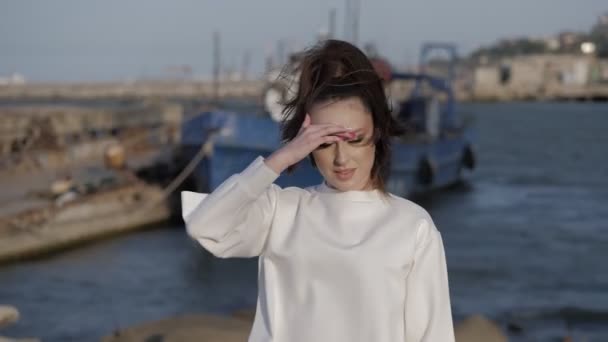 Девушка прячется от солнечных лучей против бурлящего моря и синей лодки — стоковое видео