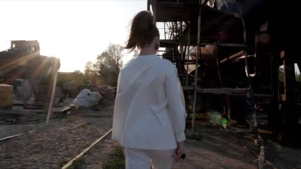 Vrouw loopt naar roestige bouw tegen stralende zon — Stockvideo