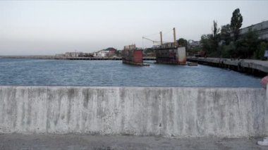 Kadın, uçsuz bucaksız gökyüzünün altında, rıhtımda yürüyor ve duruyor.
