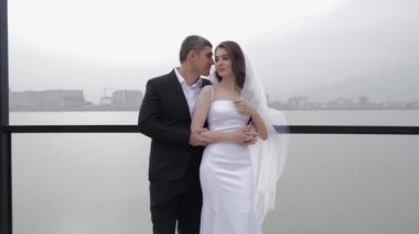 Takım elbiseli adam uzun tüylü duvağıyla lüks gelini öpüyor.