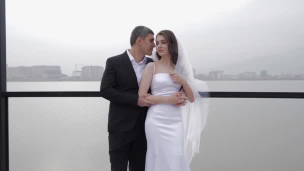 Мужчина в костюме целует роскошную невесту с длинной пушистой вуалью — стоковое видео
