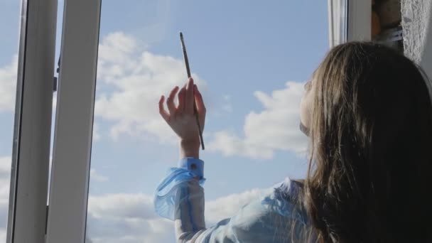 Mulher desenha nuvens no céu azul real com escova em vidro — Vídeo de Stock