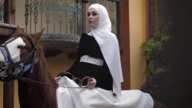 Arap kostümlü binici kadın bahçeden kestane ata biniyor.
