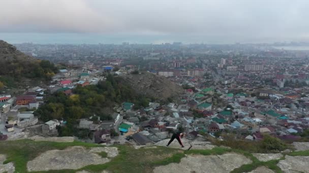 Woman jumps and stretches body standing on rock against city — Stock Video