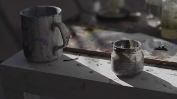 Mug and jar with paint smears on table near artist workplace — Stock Video