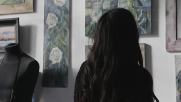 Дама розв'язує волосся проти малюнків на стіні в художній студії — стокове відео