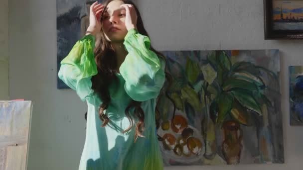 Дівчина з кучерявим волоссям в зеленій сукні позу біля картинки — стокове відео