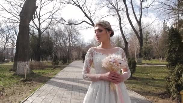 Noiva sonhadora em vestido branco detém pequeno buquê no parque — Vídeo de Stock