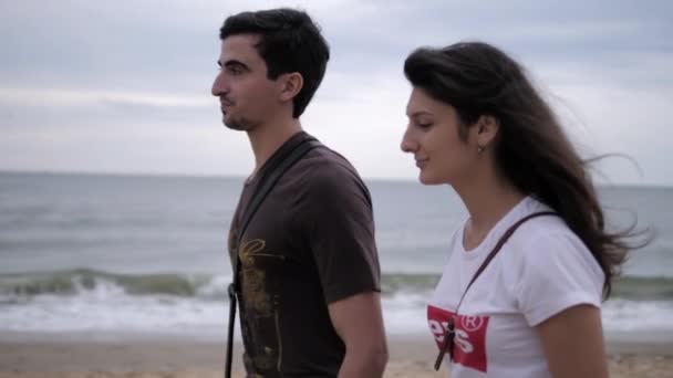 Alegre pareja camina a lo largo de la playa de mar en el día de verano ventoso — Vídeo de stock