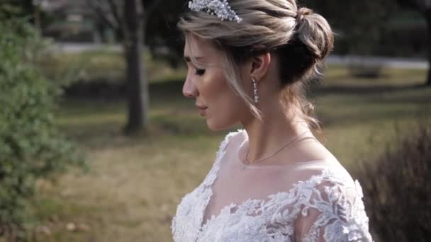 Blond brud i bröllopsklänning med mjuka snören i parken — Stockvideo