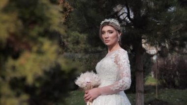 Gelin gelinliği ve taç yeşil parkta çiçek tutuyor.