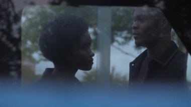 Afro-Amerikalı bir erkek ve kadın arabanın yanında birbirlerine bakıyorlar.