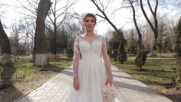 Женщина в украшенном свадебном платье держит букет в парке — стоковое видео