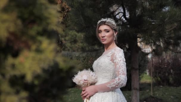 Noiva em vestido de noiva e tiara detém flores no parque verde — Vídeo de Stock