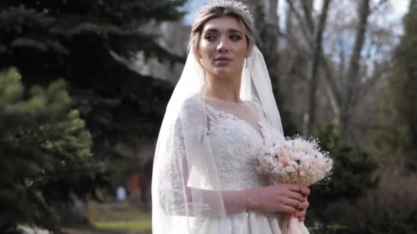 Женщина в свадебном платье с букет и вуаль в зеленом парке — стоковое видео
