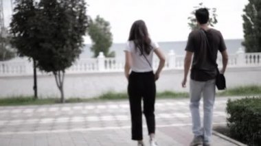 Erkek ve kadın bulutlu bir yaz gününde şehir parkında yürürler.