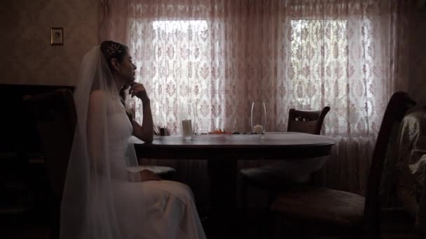 Élégante mariée en robe de mariée se trouve à table contre les fenêtres — Video