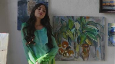 Yeşil elbiseli tembel kız çizimlerin yanında poz veriyor.