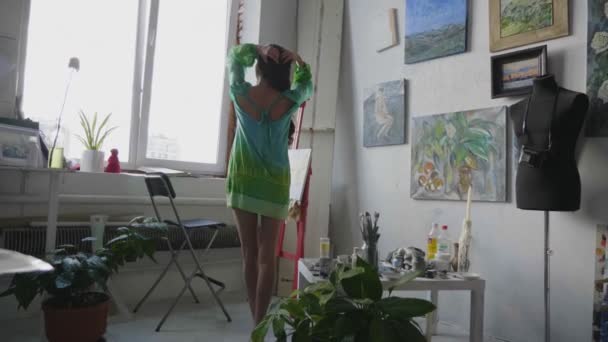 Kobieta w stylowej sukience pozuje w pobliżu okna i sztalugi w studio — Wideo stockowe