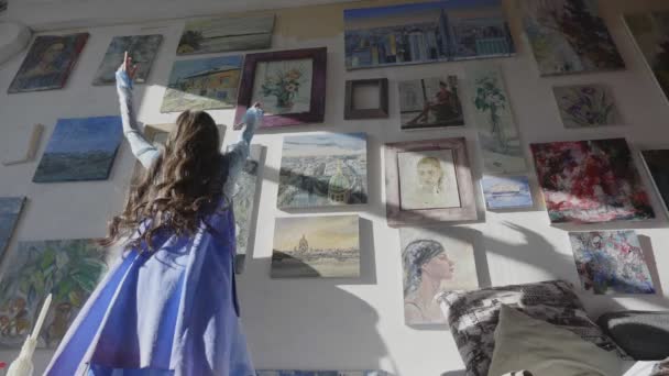 Dziewczyna artysta tańczy w pobliżu ściany ze zdjęciami przychodzącymi do sztalugi — Wideo stockowe