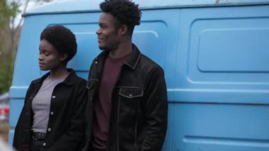 Afro-Amerikalı erkek ve kadın eski mavi minibüse yaslanıyor.