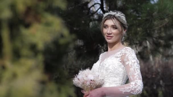 Brud med putsiga läppar i bröllopsklänning håller bukett i parken — Stockvideo