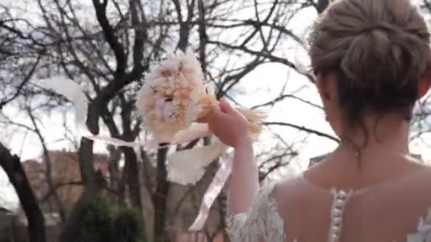 Νύφη σε δαντελωτό φόρεμα βόλτες μεταφέρουν μπουκέτο με κορδέλες — Αρχείο Βίντεο