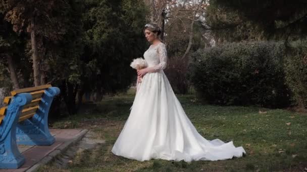 Pengantin wanita yang bijaksana dalam gaun pengantin dengan kereta api memegang karangan bunga — Stok Video