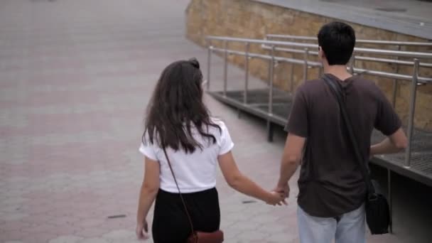 Хлопець і жінка ходять, з'єднуючи руки вздовж брукованої площі міста — стокове відео