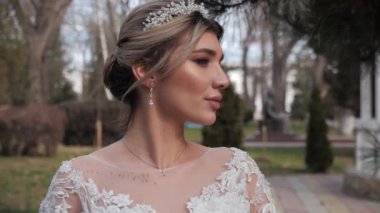 Parkta sarkık dudaklı, gelinlik ve taç giymiş pozitif gelin