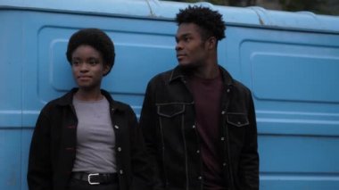Eski mavi minibüsün yanında şık ceketli Afro-Amerikan çift.