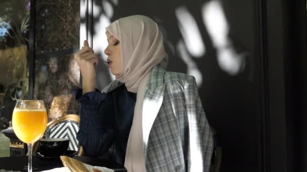 Stylish lady in hijab eats dessert with spoon in cafe — Stock Video