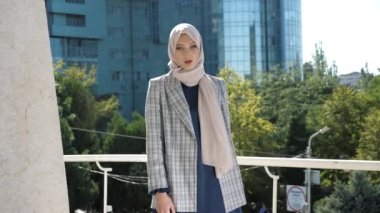 Başörtülü ve ceketli zarif bayan balkonda poz veriyor.