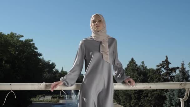 Modelo en hijab y vestido gris pone las manos en pasamanos — Vídeos de Stock