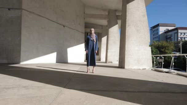 穿着长裙、头戴头巾的年轻女子站在灰色的人行道上 — 图库视频影像