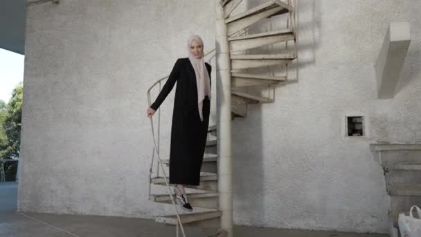 Dáma ve stylovém hidžábu jde dolů po točitém schodišti s úsměvem — Stock video