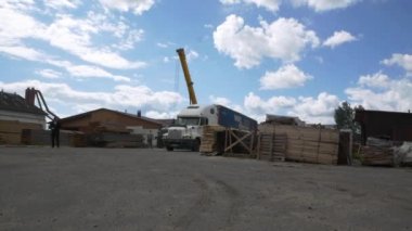 Bulutlu gökyüzünün altında tahtalar ve vinçlerle dolu bir fabrika.