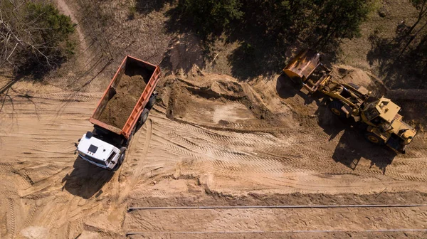 Экскаватор загружает песок в грузовик с беспилотником для аэрофотосъемки — стоковое фото