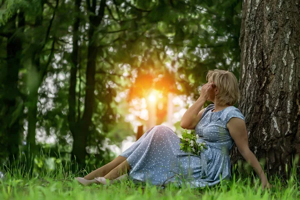 Una mujer con un vestido azul sentada cerca de un árbol y admira los soles — Foto de Stock