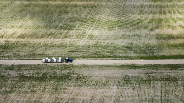 tractor rides on the field and carries bales of hay aerial view