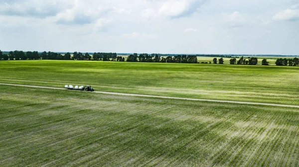 tractor rides on the field and carries bales of hay aerial view